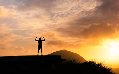 People, power, strength, and determination.  Strong man flexing his muscles against sunset. 