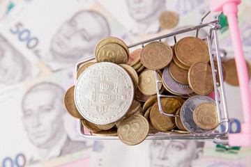 Bitcoin and coins in shopping cart on hryvnia banknotes background