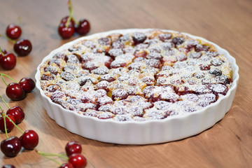 Clafoutis with cherry in ceramic form. Clafoutis cherry pie on rustic wooden background.