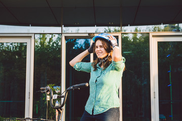 Theme to work on the bike. A young Caucasian woman arrived on environmentally friendly transport bike to the office. Girl in a bicycle parking office building in a helmet, gloves and shirt and jeans