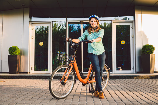 Theme to work on the bike. A young Caucasian woman arrived on environmentally friendly transport bike to the office. Girl in a bicycle parking office building in a helmet, gloves and shirt and jeans