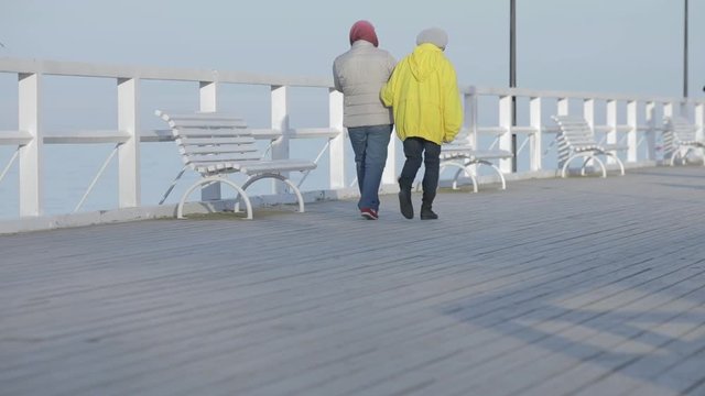 An older couple walks down a seaside boardwalk on a cold day