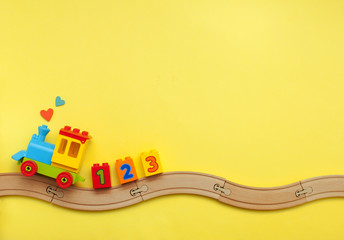 Kids toy train with numbers on toy wooden railway on yellow background with copy space