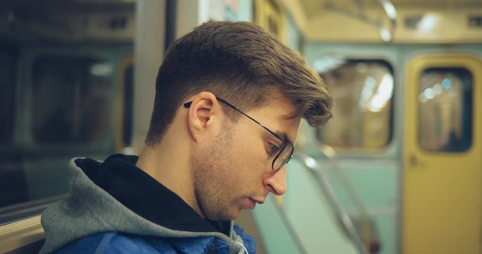 Young guy with glasses rides in an empty transport and carefully looks. Side view. Close-up.