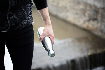 Close-up of man hand holding steel bottle for water, on river background