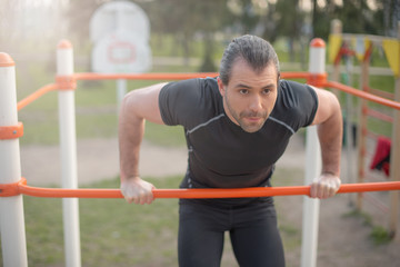 Fototapeta na wymiar handsome man in the summer outdoors on the playground doing an exercise on the horizontal bar
