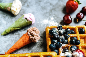 Sweet waffles with tasty red fruits full of healthy vitamins with some ice creams with waffle, over blue stone background with copy space for text.
