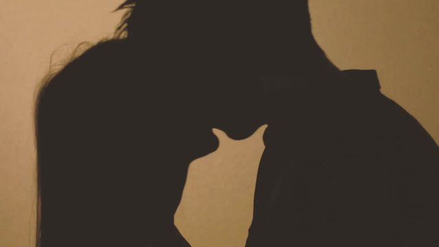 Affectionate and tender couple embrace. Love expression. Young man and woman kiss in the shadow