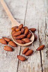 Organic fresh almond seeds on wooden spoon closeup on rustic wooden table.