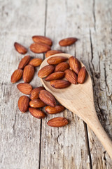 Fresh raw almond seeds on wooden spoon closeup on rustic wooden table.