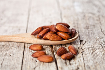 Organic fresh almond seeds on wooden spoon closeup on rustic wooden table.