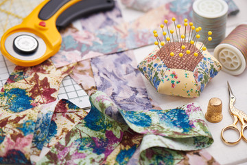 Brightly colored strips of fabric, rotary cutter, pin cushion and quilting accessories on white wooden surface