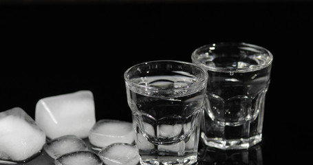 Vodka in shot glasses with ice cubes placed on a black background
