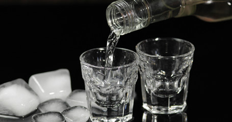 Pour vodka into shot glasses with ice cubes placed on a black background