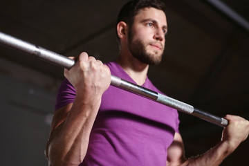 Young healthy sporty athletic man in the gym performing biceps curls with a barbell and doing arms exercises. Training in fitness studio