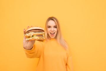 Happy girl in an orange casual clothing holds a great tasty burger in his hands and shows him in a...