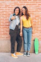 Young women couple making a selfie. Behind brick wall. Positive emotion and tolerance concept.