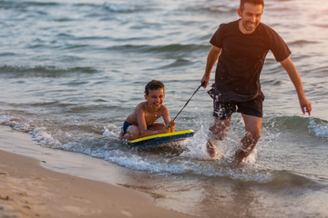 Father and son surfing on boogie boards on the sunset