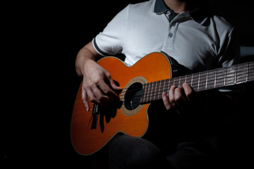 Man playing an acoustic guitar on a dark background. Playing guitar