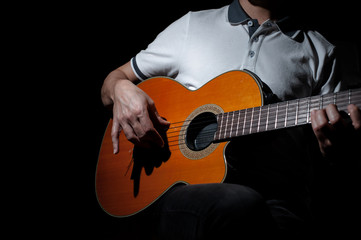Man playing an acoustic guitar on a dark background. Playing guitar