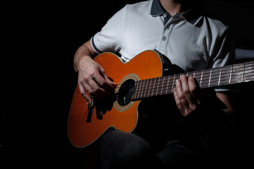 Man playing an acoustic guitar on a dark background. Playing guitar