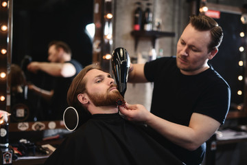 Barbershop concept. Handsome hairdresser cutting hair of male client. Hairstylist serving client at barber shop.