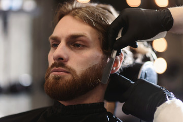 Closeup of barber shaving man beard with straight steel razor blade at barbershop. Brutal hairdresser at work