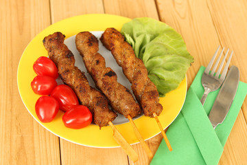 delicious grilled meat on fried skewers lies on a yellow plate with fresh vegetables, tomatoes, salad