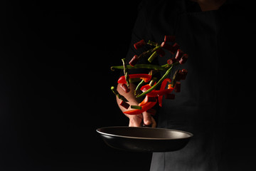 Chef is cooking pepperoni sausages with sweet pepper and spriykovoy beans, on a black background, a...