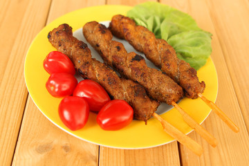 delicious grilled meat on fried skewers lies on a yellow plate with fresh vegetables, tomatoes, lettuce, on a light wooden background