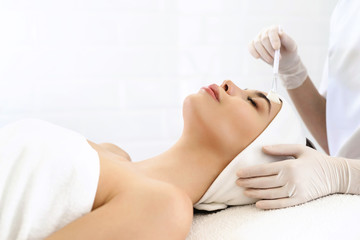 Obraz premium Model in white headband bandage cap lying on couch with closed eyes. Hand of beautician doctor in white glove touching her face with brush. Head and shoulders, healthcare, cosmetology, beauty clinic