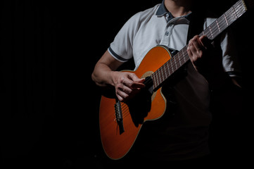 Man playing an acoustic guitar on a dark background. Playing guitar