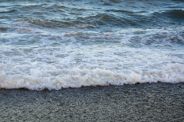 Colorful seascape, white foam of wave on beach close up