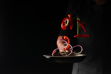 Chef preparing pepperoni sausages with green beans, sweet bell peppers and red onion rings, on a...