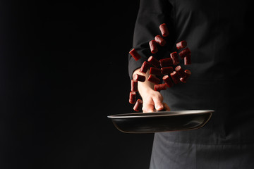 Chef preparing pepperoni sausages, on a black background, horizontal photo