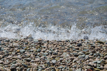 Background of seashore, pebble beach and transparent sea close up