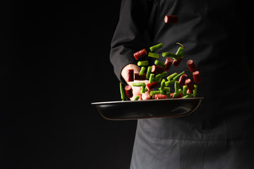 Chef is cooking pepperoni sausages with green beans, on a black background, a recipe book, German...