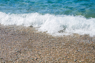 Summer background. Colorful coast with sea wave. View of the pebble beach and clear turquoise water
