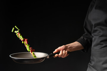 Chef is cooking pepperoni sausages with sweet pepper and spriykovoy beans, on a black background, a...