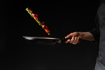 Chef is cooking pepperoni sausages with sweet pepper and spriykovoy beans, on a black background, a...