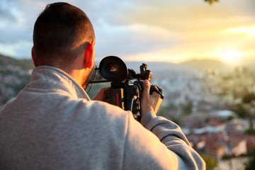 video camera, cameraman, sunset. The photographer records the sunset in the background of a beautiful city