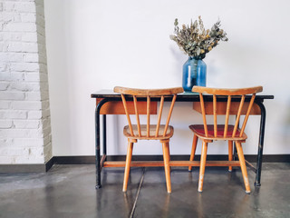 Vintage wooden elementary school desk and two wooden chairs with a dried flower arrangement in a blue vase against a white wall