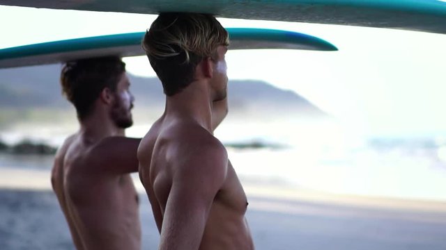 Portrait of two handsome surfer guy friends with surfboards looking at waves to surf. Concept of millennial men friends surfing adventure travel.  