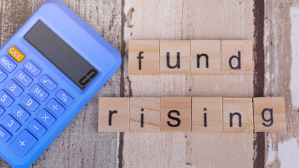 Concept image of Fund Rising. Word abstract in vintage letterpress wood type blocks with a blue calculator over nice wooden textured background