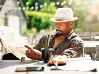 mature african american man reading newspaper in outside patio