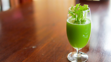 Fresh green celery juice in glass on wooden brown background