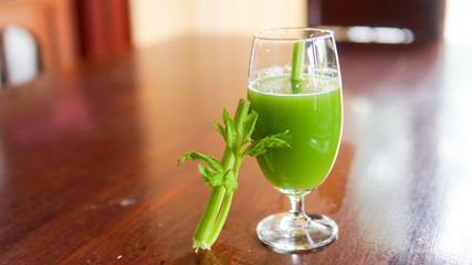 Fresh green celery juice in glass on wooden brown background