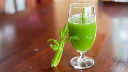 Fresh green celery juice in glass on wooden brown background