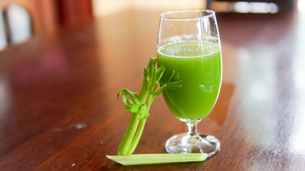 Fresh green celery juice in glass on wooden brown background