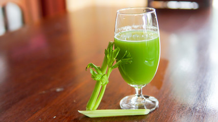 Fresh green celery juice in glass on wooden brown background